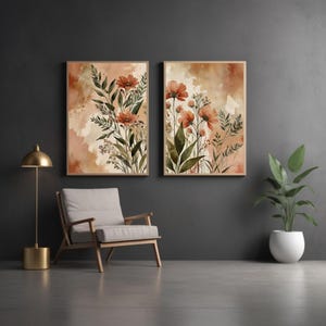 Puede incluir: Dos impresiones enmarcadas de acuarela floral. Cada impresión presenta flores naranjas y follaje verde sobre un fondo suave y neutro. La obra de arte se exhibe en una habitación con una silla, una lámpara de pie y una planta en maceta, creando un ambiente sereno.