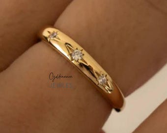 May include: A gold ring with three star-shaped diamond accents. The ring has a smooth, polished surface and a rounded shape. The ring is a size 7.