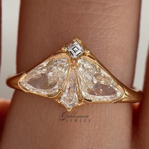 May include: A gold ring featuring a unique design with three large, clear, diamond-shaped stones and a small square diamond at the top. The ring has a delicate, intricate setting. The brand name "Goldenaura Jewels" is visible.