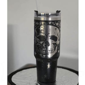Puede incluir: Vaso de acero inoxidable negro con un diseño de calavera plateada y detalles de estrellas. El vaso incluye una tapa transparente y una pajita reutilizable. Un artículo de bebida único y elegante.