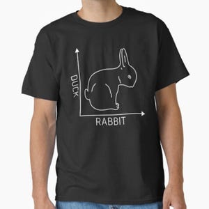 May include: Black t-shirt featuring a white line drawing of a rabbit within a graph. The graph's axes are labeled "Duck" and "Rabbit". The design is a humorous take on the classic optical illusion.