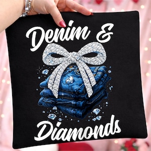 May include: Black pillow with the text "Denim & Diamonds" in white script. A sparkling diamond bow sits above a stack of blue denim jeans. Scattered diamond accents complete the design.
