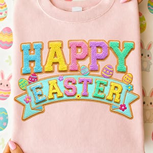 May include: A light pink sweatshirt with the words "HAPPY EASTER" in colorful, textured lettering. The text is embroidered with a 3D effect, and the word "EASTER" is on a light blue banner with Easter egg and flower accents.