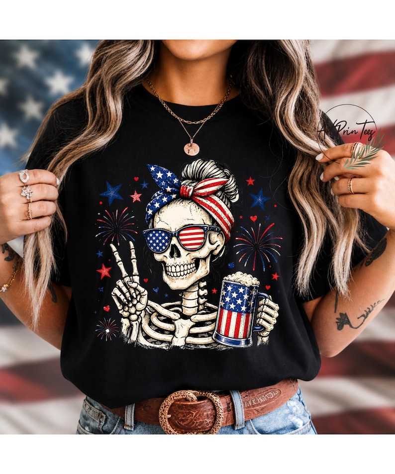 May include: Black t-shirt featuring a skeleton wearing sunglasses and a headband with an American flag design. The skeleton is holding a beer mug with an American flag design and making a peace sign. Fireworks and stars are in the background.