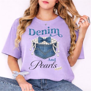Puede incluir: Camiseta lila con la frase "Denim and Pearls". El diseño presenta un bolsillo vaquero lleno de perlas y un lazo azul. La camiseta es de corte holgado.