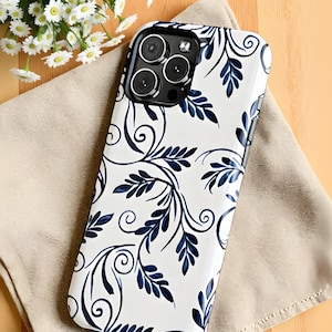 May include: White and navy blue floral patterned phone case. The case features a glossy finish and a detailed design of swirling leaves and vines. The phone case is on a beige cloth.