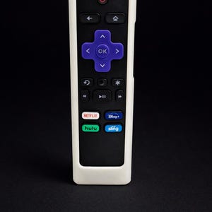 May include: A black Roku remote control with a white protective case. The remote has a purple directional pad with an "OK" button, and buttons for Netflix, Hulu, Disney+, and Sling. The power button is red.
