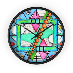 May include: A round wall clock with a black frame. The clock face features a colorful abstract design with geometric shapes, including triangles, circles, and a central square. The hands are black, and the background is light blue.