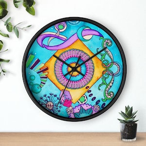 May include: A round wall clock with a black frame. The clock face features a colorful abstract design with a central orange square, a purple circle, and blue and green accents. The clock hands are black.