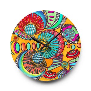 Puede incluir: Un reloj de pared redondo con un diseño abstracto vibrante. La esfera del reloj presenta un fondo amarillo con formas coloridas dibujadas a mano en rojo, azul, verde y rosa. Las manecillas negras indican la hora.