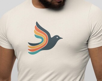 Puede incluir: Camiseta color crema con un diseño de pájaro estilizado en vuelo. El pájaro es azul oscuro con alas en colores arcoíris: turquesa, naranja y amarillo. La camiseta es de material suave, ideal para uso casual.