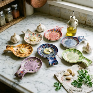 May include: A collection of seven ceramic garlic graters featuring colourful, intricate floral patterns. Each round grater has a small handle and a textured centre for grating garlic. The set includes various colours such as yellow, blue, green, and purple.