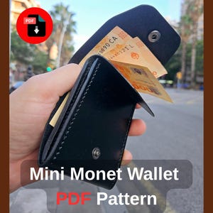 Puede incluir: Un mini monedero de cuero negro, abierto para mostrar billetes. El monedero se sostiene en una mano contra un fondo borroso al aire libre. El texto "Mini Monet Wallet PDF Pattern" es visible.