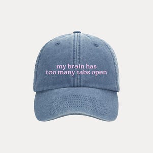 Pode incluir: Boné de beisebol de ganga azul com a frase "my brain has too many tabs open" em letras cor-de-rosa. O boné tem uma aba curva e uma alça ajustável na parte de trás.