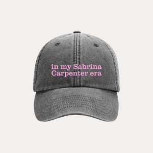 May include: A gray baseball cap with the text "in my Sabrina Carpenter era" in pink lettering. The cap has a curved brim and a structured crown, suitable for casual wear.