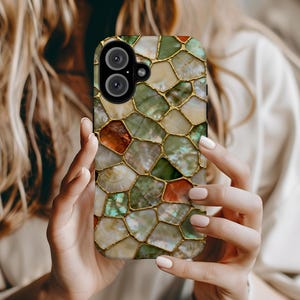 May include: A smartphone case with a mosaic design. The case features a pattern of irregularly shaped pieces in shades of green, white, and orange, outlined with gold. The phone case has a dual-lens camera.