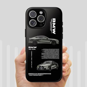 Op de afbeelding: Zwarte telefoonhoes met twee zilveren BMW auto-illustraties. De hoes bevat de tekst "BMW MOTORSPORT GERMAN MADE" en "BMW M4 CSL". Het ontwerp bevat ook de tekst "MINERAL GREY METALLIC" en "GERMAN ENGINEERING MOTORSPORT".