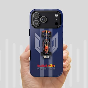 May include: A navy blue phone case with a Formula 1 race car design. The case has a dark blue background with a silver stripe and a Red Bull Racing logo. The phone case is held in a hand.
