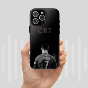 K&ouml;nnte beinhalten: Schwarze Handyh&uuml;lle mit einem Graustufenbild eines Fu&szlig;ballspielers von hinten, der ein Trikot mit der Nummer 7 und dem Namen "RONALDO" tr&auml;gt. Die H&uuml;lle hat auch die Buchstaben "CR7" und eine Unterschrift.