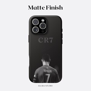 K&ouml;nnte beinhalten: Schwarze, matte Handyh&uuml;lle mit einem Graustufenbild eines Fu&szlig;ballspielers, der "Ronaldo" und die Nummer "7" auf dem Trikot zeigt. Die H&uuml;lle zeigt auch den Text "CR7" und "ELURA STUDIO".