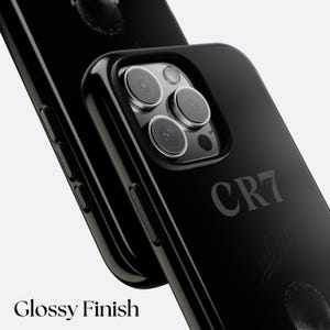 K&ouml;nnte beinhalten: Schwarze Handyh&uuml;lle mit gl&auml;nzendem Finish. Das Geh&auml;use tr&auml;gt den Text "CR7" und eine Unterschrift. Das Bild enth&auml;lt auch den Text "Glossy Finish". Die Handyh&uuml;lle dient zum Schutz der Kamera des Telefons.