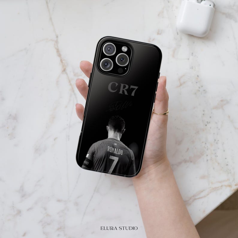 K&ouml;nnte beinhalten: Schwarze Handyh&uuml;lle mit dem Text "CR7" und einem Graustufenbild eines Fu&szlig;ballspielers mit der Nummer 7 auf seinem Trikot. Die H&uuml;lle hat eine gl&auml;nzende Oberfl&auml;che und einen Kameraausschnitt.