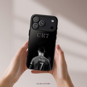 K&ouml;nnte beinhalten: Schwarze Handyh&uuml;lle mit einem Graustufenbild eines Fu&szlig;balltrikots mit der Nummer 7 und dem Namen Ronaldo. Die H&uuml;lle zeigt auch "CR7" und eine Unterschrift. Die Handyh&uuml;lle hat ein schwarzes Kameramodul.