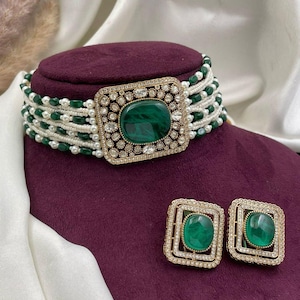 Peut inclure: Un ensemble collier ras du cou et boucles d'oreilles assorties. Le ras du cou présente une pierre centrale carrée vert émeraude entourée de cristaux transparents et d'un cadre doré. Le collier est orné de perles blanches et de perles vertes. Les boucles d'oreilles ont des pierres vert émeraude assorties.