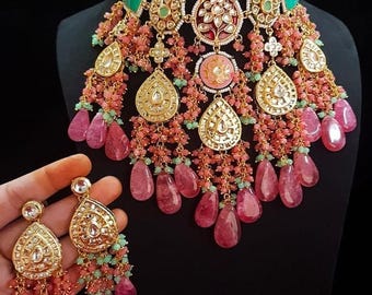 May include: A detailed gold necklace and earring set. The necklace has pink, green, and gold elements, with teardrop and circular pendants. The earrings echo the necklace's design, with hanging pink and green beads.