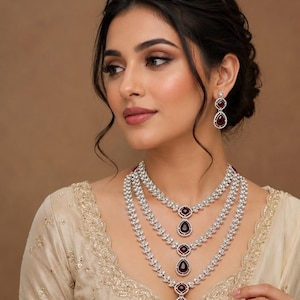 Peut inclure: Un ensemble composé d'un collier à trois rangs et de boucles d'oreilles pendantes assorties, en métal argenté, serti de pierres transparentes et de pierres centrales rouge foncé en forme de poire, avec des pendentifs en goutte d'eau.