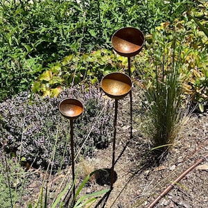 Puede incluir: Tres estacas de jard&iacute;n de metal color &oacute;xido, cada una con una parte superior peque&ntilde;a, poco profunda y en forma de cuenco. Las estacas est&aacute;n dispuestas a diferentes alturas, con tallos verticales delgados que sostienen los cuencos.