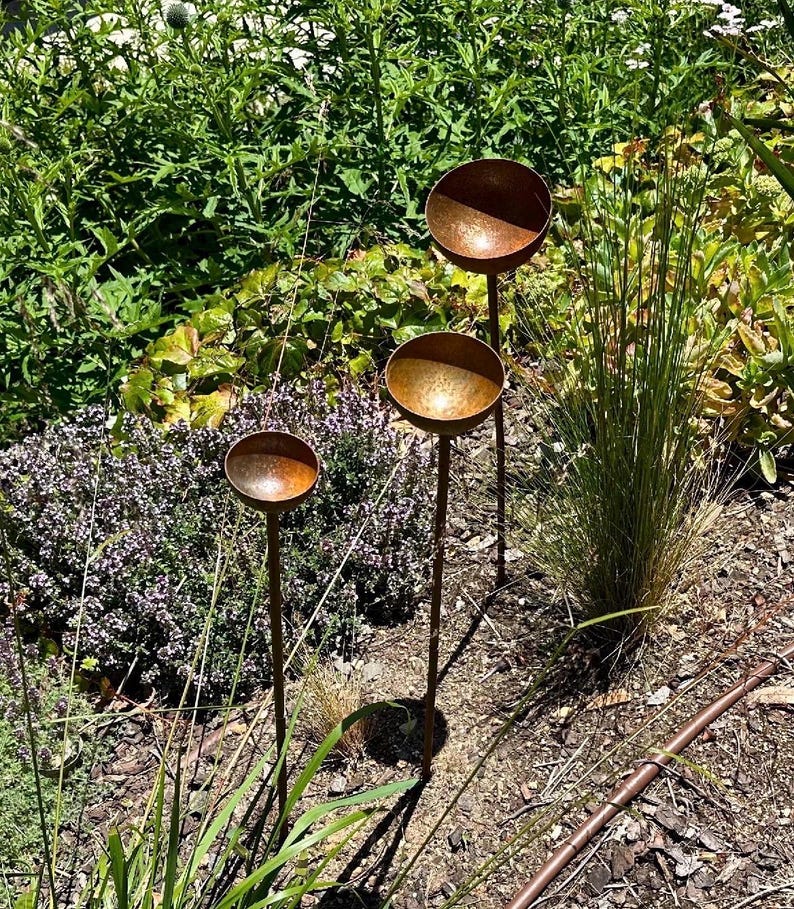 Puede incluir: Tres estacas de jard&iacute;n de metal color &oacute;xido, cada una con una parte superior peque&ntilde;a, poco profunda y en forma de cuenco. Las estacas est&aacute;n dispuestas a diferentes alturas, con tallos verticales delgados que sostienen los cuencos.