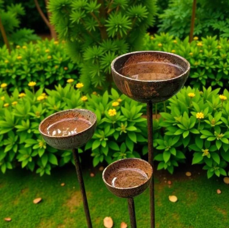 Puede incluir: Tres cuencos de jard&iacute;n de color marr&oacute;n oscuro a distintas alturas, cada uno lleno de agua. Los cuencos est&aacute;n montados sobre finas varillas met&aacute;licas oscuras, creando una disposici&oacute;n escalonada. Las superficies de los cuencos parecen texturizadas.