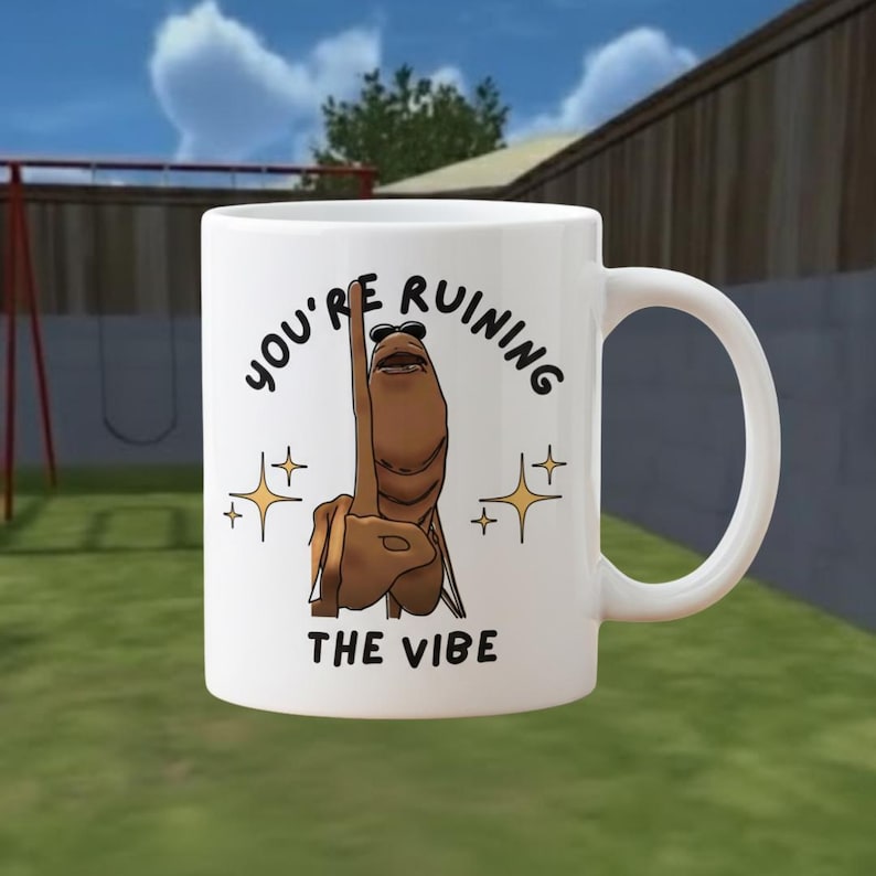 May include: White ceramic mug with a humorous design. The mug features a cartoon character with sunglasses giving the middle finger, accompanied by the text "YOU'RE RUINING THE VIBE" and star accents. The mug has a curved handle.
