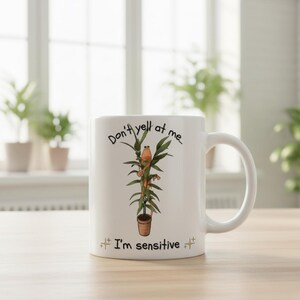 May include: White ceramic mug with a humorous plant-themed design. The mug features a cartoon plant with a face and the text "Don't yell at me... I'm sensitive." The design includes a brown pot and green leaves.