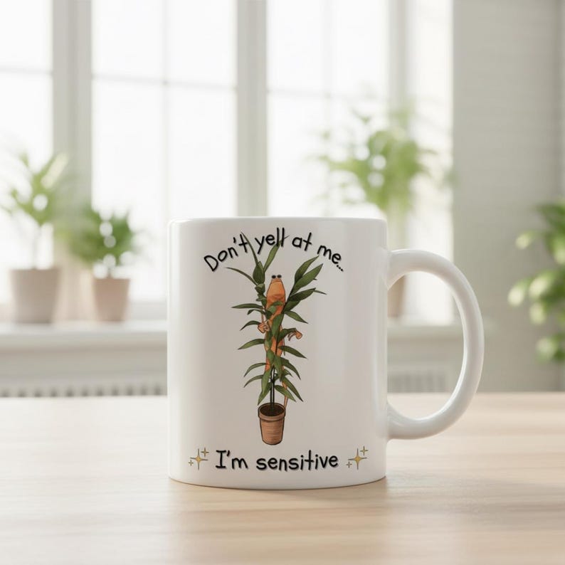 May include: White ceramic mug with a humorous plant-themed design. The mug features a cartoon plant with a face and the text "Don't yell at me... I'm sensitive." The design includes a brown pot and green leaves.