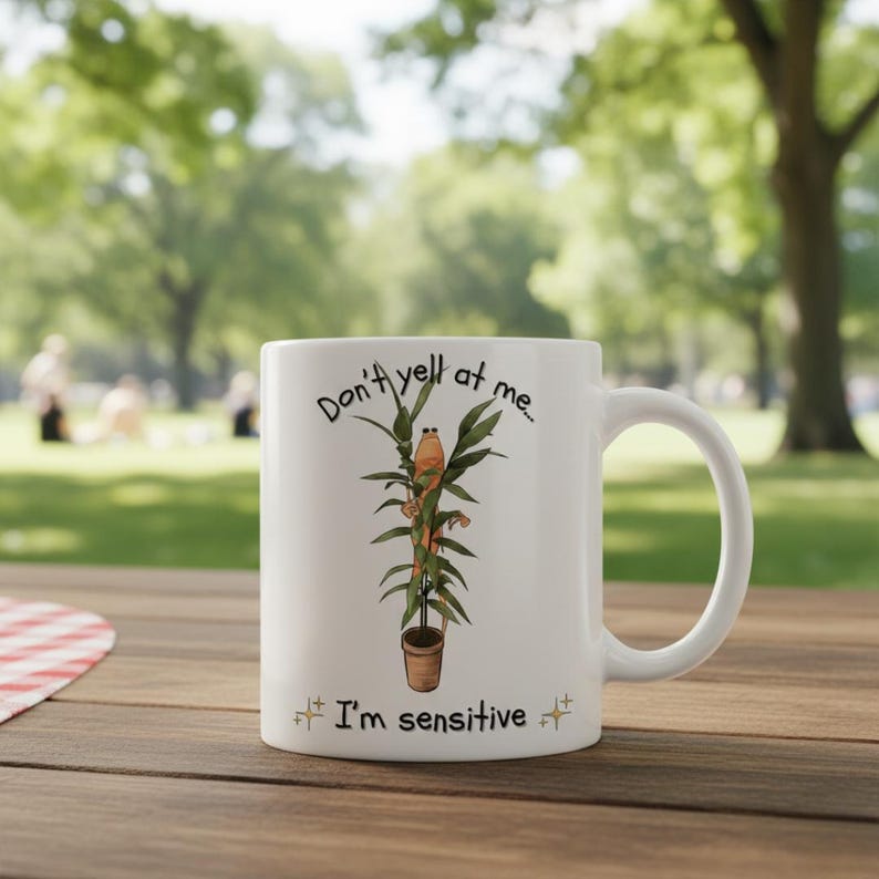 May include: White ceramic mug with a humorous design. The mug features the text "Don't yell at me... I'm sensitive" along with an illustration of a cartoon frog on a plant. The mug has a curved handle and is suitable for hot or cold beverages.