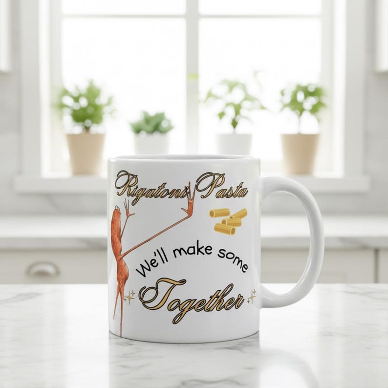 May include: White ceramic mug with the words "Rigatoni Pasta" and "We'll make some Together" in a decorative font. The mug features an illustration of a pasta shape and a person-like pasta figure.