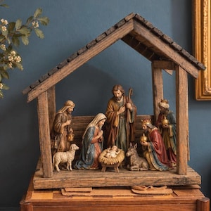 May include: A wooden nativity scene set featuring figurines of Mary, Joseph, the infant Jesus in a manger, a shepherd with a sheep, and three wise men. The figures are housed within a rustic, open-sided wooden stable structure with a gabled roof.
