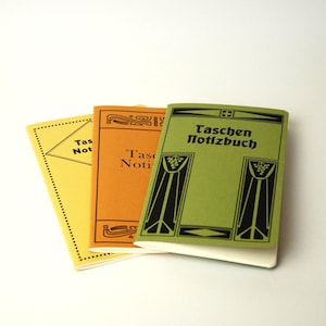 Könnte beinhalten: Drei kleine Notizbücher mit Papierumschlägen in Gelb, Orange und Grün. Jeder Umschlag zeigt den schwarzen Aufdruck "Taschen Notizbuch" sowie dekorative schwarze grafische Ränder. Die Notizbücher sind leicht fächerförmig angeordnet.
