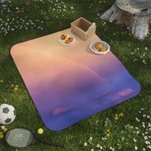 May include: A picnic blanket with a gradient design of orange, pink, and purple, resembling a sunset or rainbow. A soccer ball, tennis racket, and food items are on the grass. A woven basket and a plate of fruit are on the blanket.