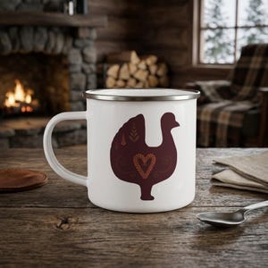 May include: A white enamel mug with a silver rim featuring a dark maroon silhouette of a turkey. The turkey design includes a central heart shape and small leaf-like patterns in a lighter shade of brown, centred on the front of the mug.