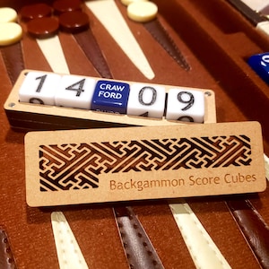 May include: A backgammon set with brown and cream-coloured game pieces. A wooden score cube holder displays the numbers 1, 4, 0, and 9, with a blue cube reading "Craw Ford." A wooden sign below reads "Backgammon Score Cubes."