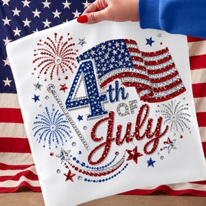 Puede incluir: Cojín cuadrado blanco con un diseño patriótico. El diseño presenta el texto "4th of July" en rojo y azul, junto con una bandera americana brillante y fuegos artificiales. El cojín se sostiene frente a una bandera americana.