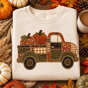 Könnte beinhalten: Ein cremefarbenes Sweatshirt mit Rundhalsausschnitt und einem zentralen Motiv eines Lastwagens, der zwei Kürbisse transportiert. Das LKW-Design besteht aus verschiedenen Stoffmustern wie Schottenkaro, Leopardenmuster, Vichy-Karo und Olivgrün.