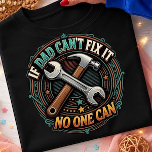 May include: A black t-shirt featuring a circular graphic with a crossed hammer and wrench. The text reads IF DAD CAN'T FIX IT NO ONE CAN in a bold, multi-coloured font. The design includes concentric circles and small star accents in teal, orange, and white.