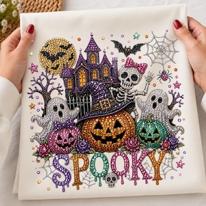 May include: A white fabric canvas featuring a diamond painting design of a Halloween scene. It includes a purple haunted house, a yellow moon, a skeleton with a pink bow, ghosts, pumpkins, a bat, a spider web, and the word SPOOKY in colorful letters.