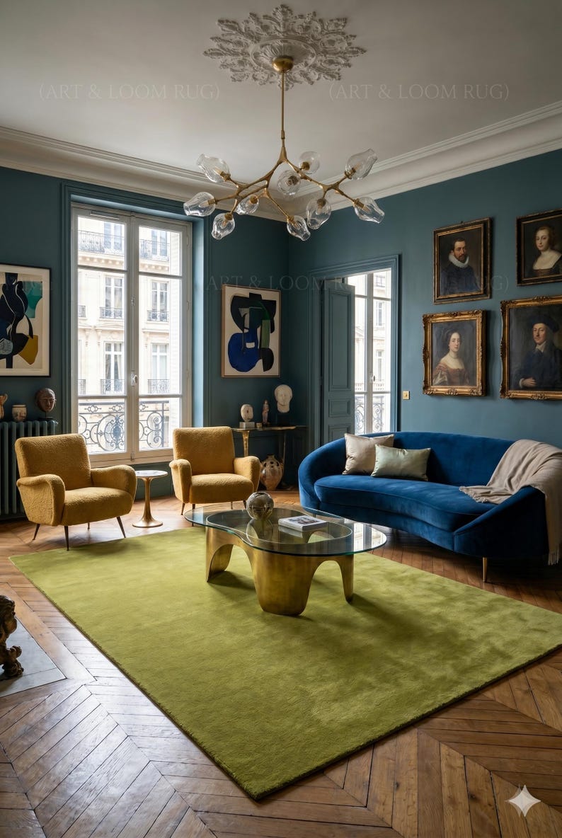 May include: A living room with a green rug, blue sofa, and two yellow armchairs. The room has a gold coffee table, artwork, and a chandelier. The walls are teal, and the floor is hardwood.