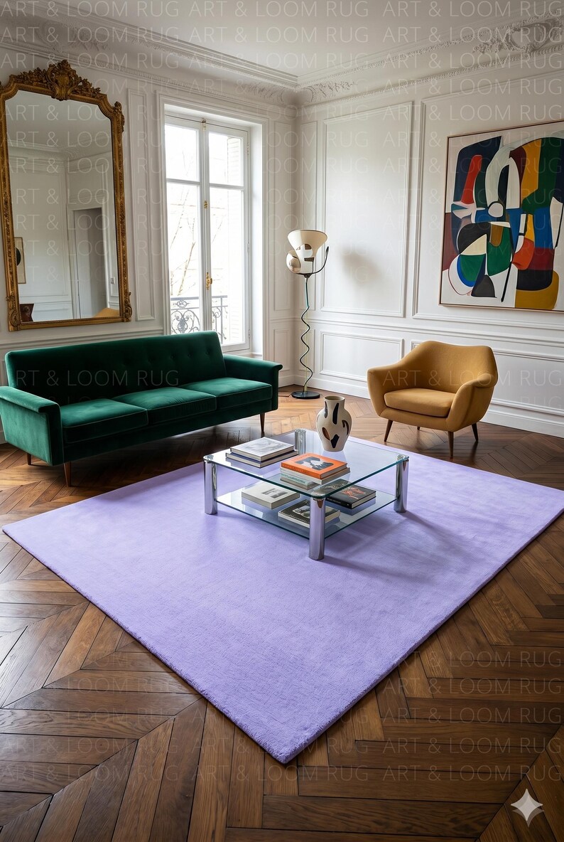 May include: A large, rectangular, light purple rug in a living room setting. The rug is placed on a herringbone patterned hardwood floor. A green velvet sofa, a yellow armchair, and a glass coffee table are also visible.