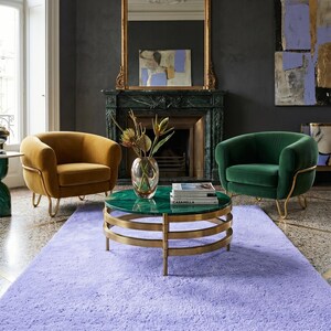 May include: A luxurious living room setting featuring a lavender rug, two velvet armchairs in gold and green, and a round coffee table with a green top and gold base. A fireplace and ornate mirror complete the elegant decor.